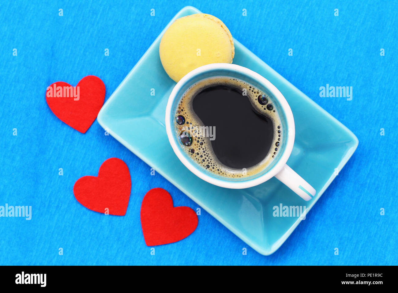 Black coffee in cup, lemon macaroon and three red hearts on blue surface Stock Photo