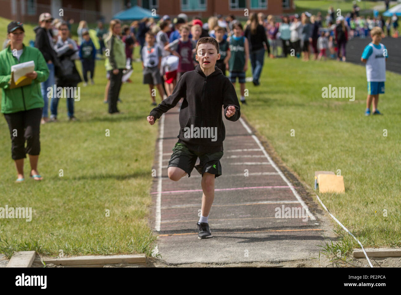 Young boy competing in track & field's  trple jump, wearing hoodie and shorts. Determinded look as he prpares to take jump. Model released Stock Photo