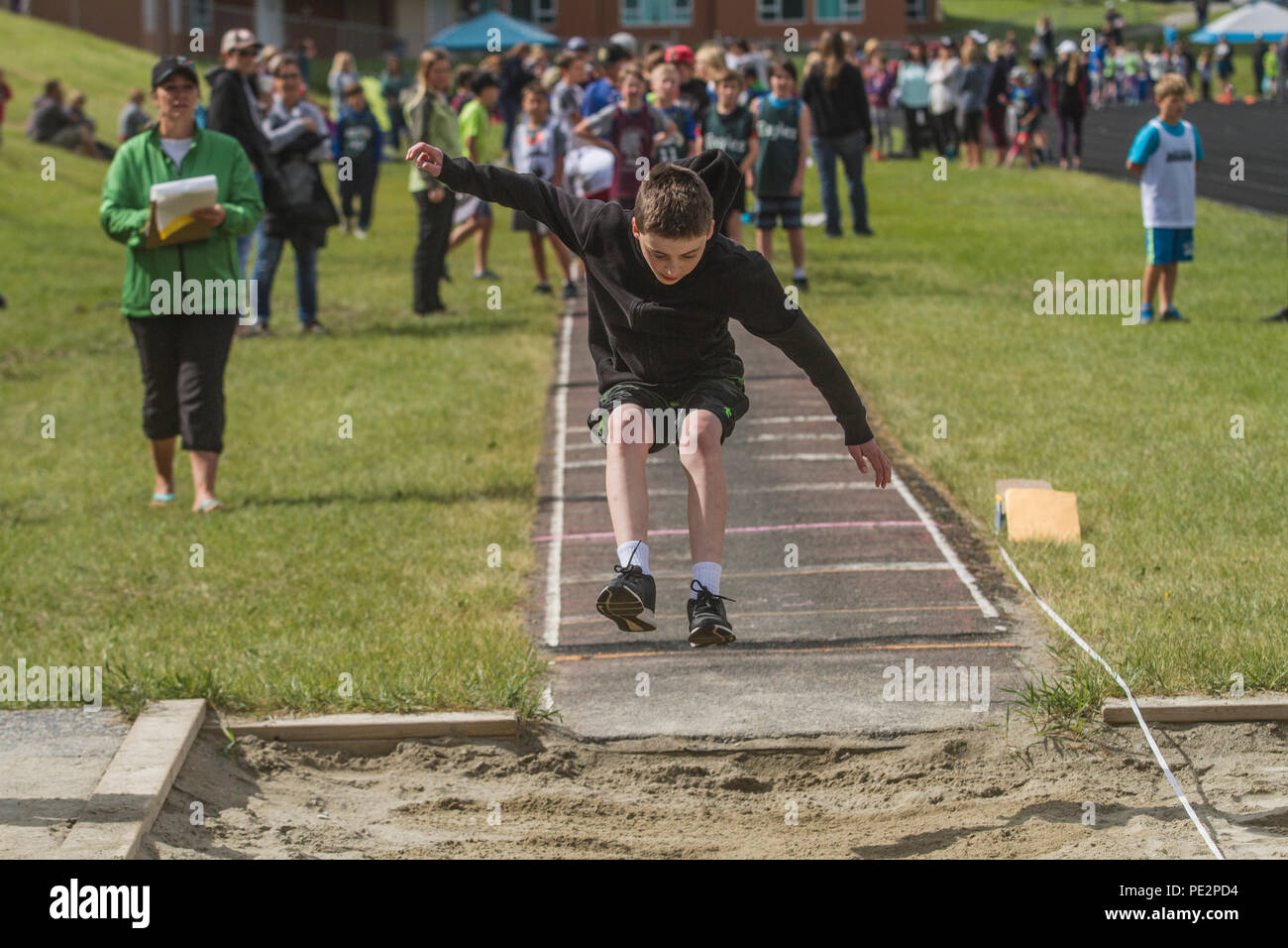 Young boy competing in track & field's  trple jump, wearing hoodie and shorts. Caught in mid air. Model released Stock Photo