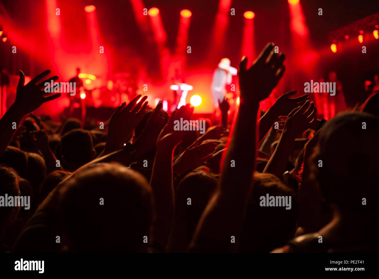 concert crowd during festival, hands of many people cheering musicians playing music on stage, red back light Stock Photo