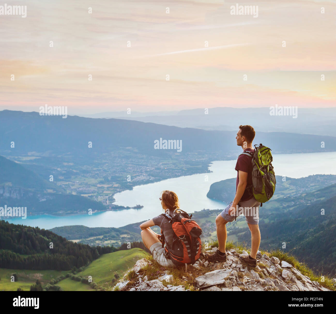 couple of hikers relaxing on top of mountain with beautiful panoramic view outdoors, two tourists backpackers during hike, adventure honeymoon Stock Photo