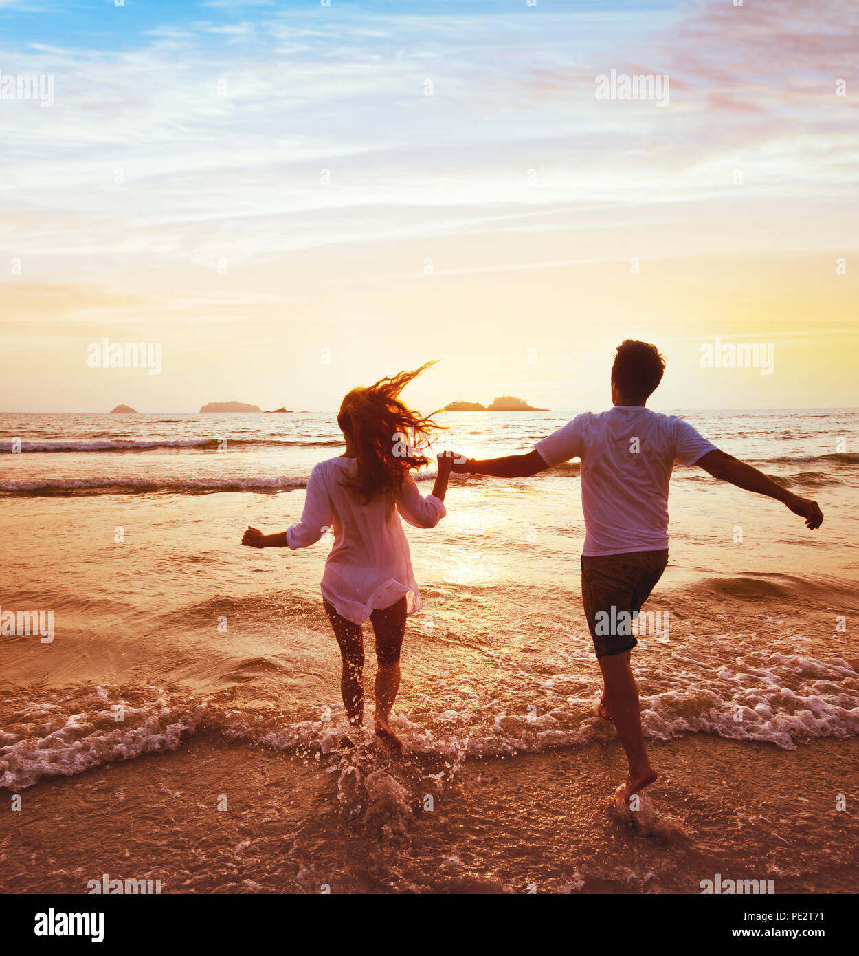 happy couple on honeymoon vacation travel, romantic dream beach holidays, happiness background, silhouettes of man and woman running to the sea at sun Stock Photo