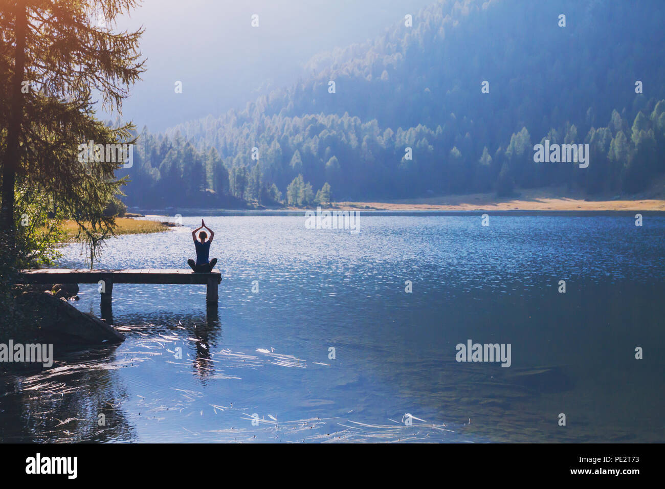yoga beautiful background, harmony in life, meditation practice, silhouette of woman sitting in lotus position on the pier of lake and doing breathing Stock Photo