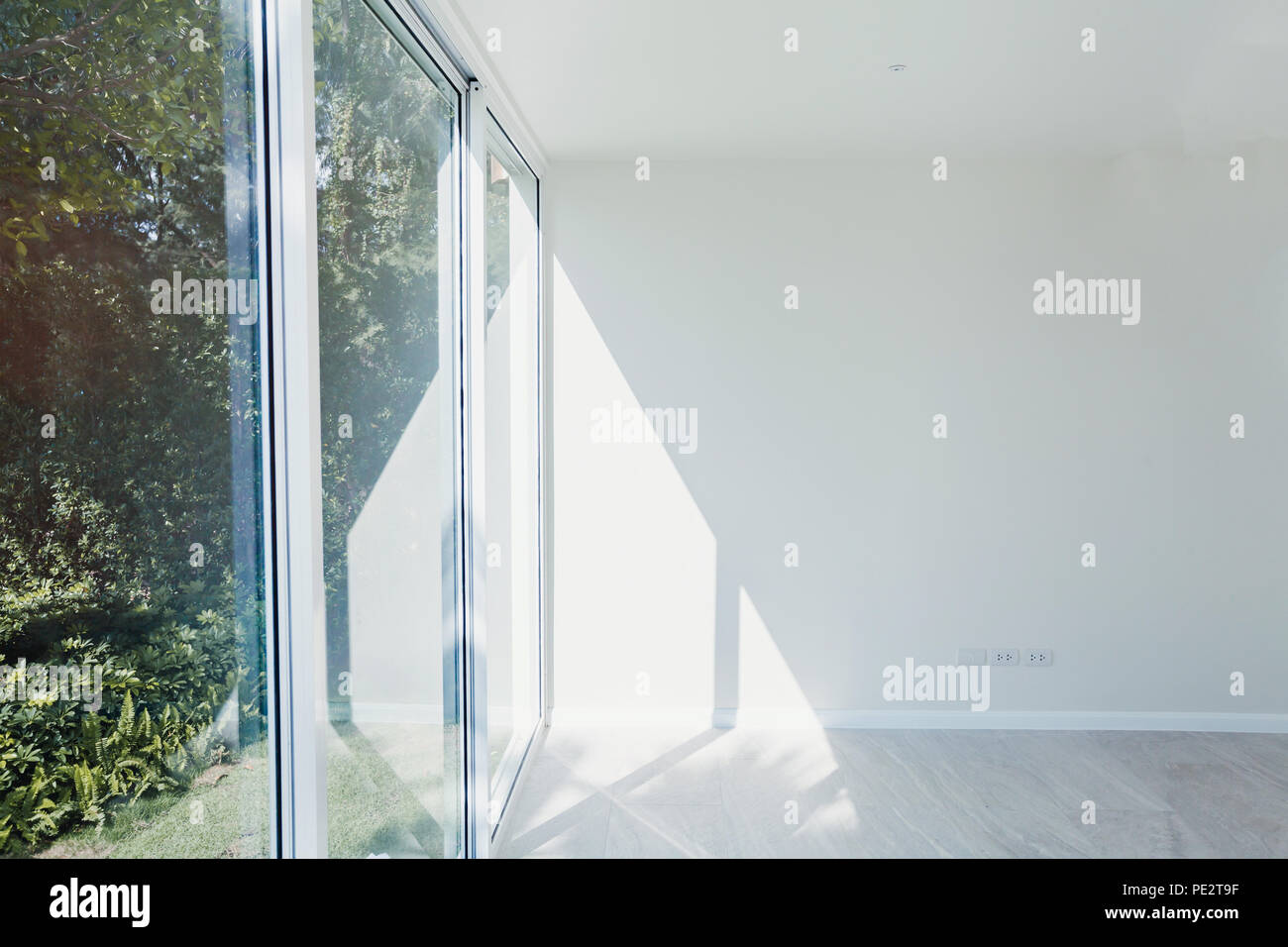 empty sunny room interior with white painted wall, big window and modern wooden floor parquet, new apartment under construction Stock Photo