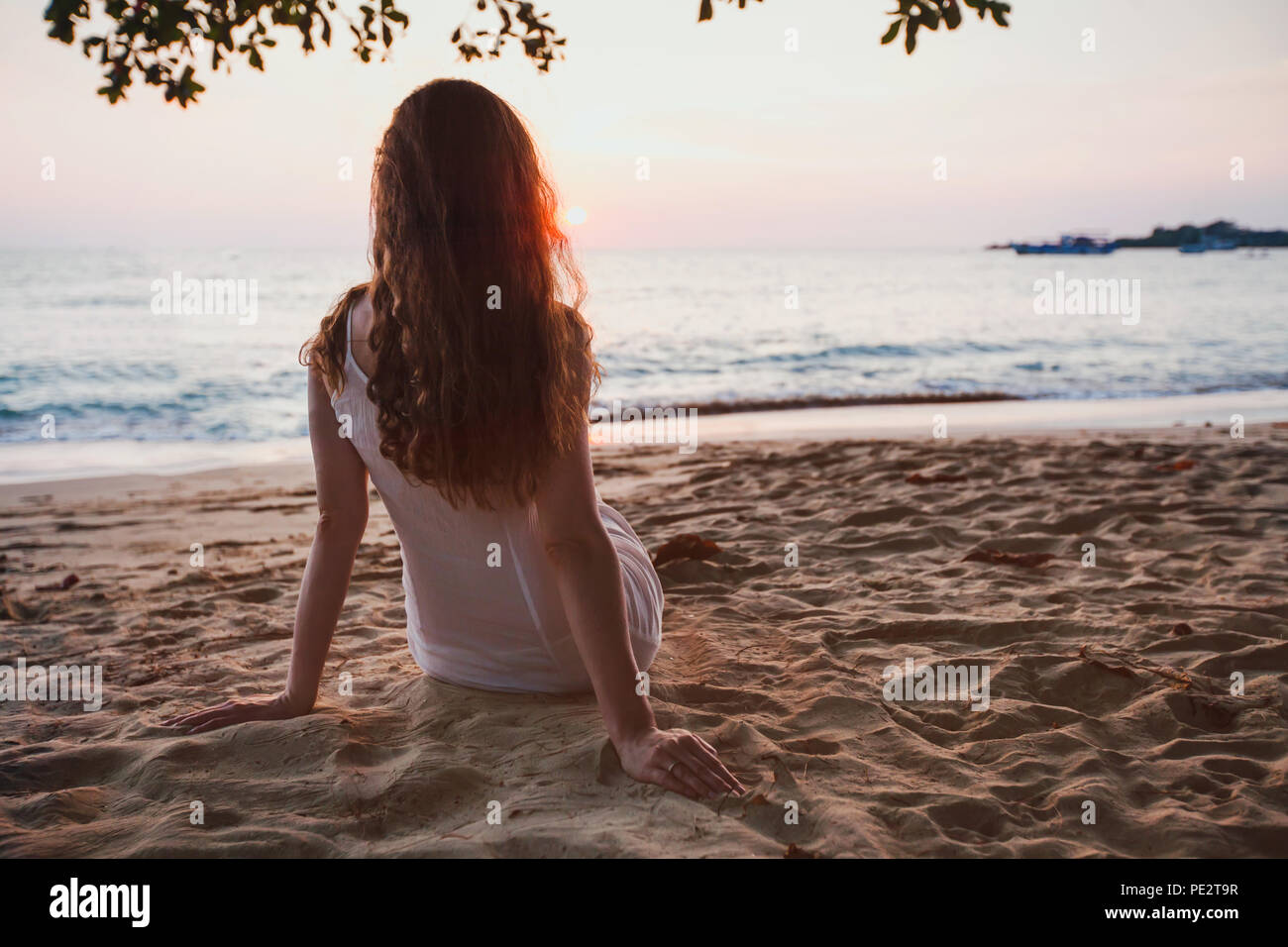 romantic dreams, beautiful girl sitting alone on calm quiet sunset beach, relaxation Stock Photo