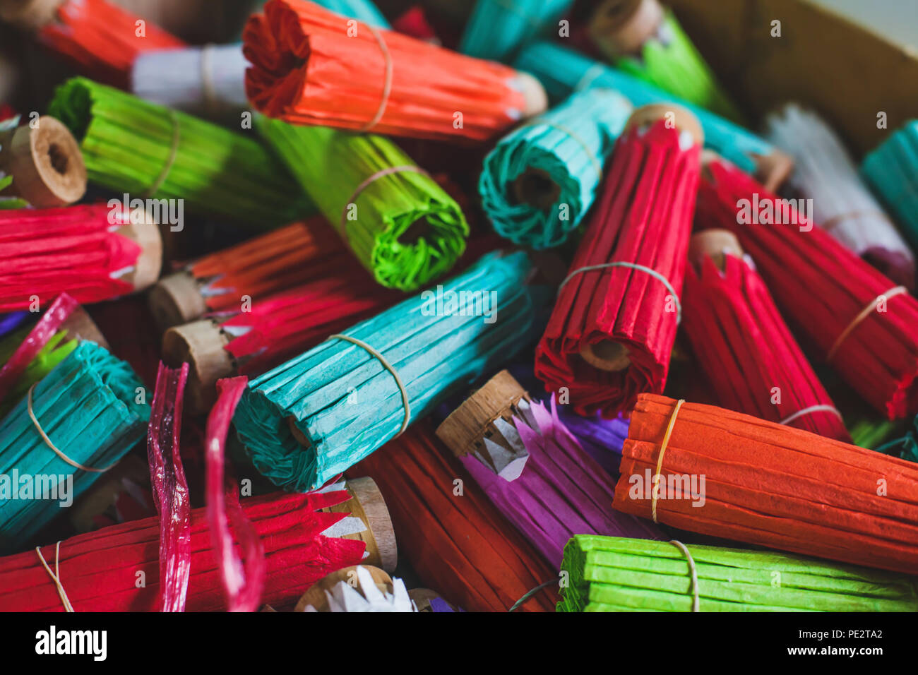 colorful traditional paper craft multicolored umbrellas in thai shop for sale, craftsmanship in Thailand, Chiangmai, rolls of different colors, red, c Stock Photo