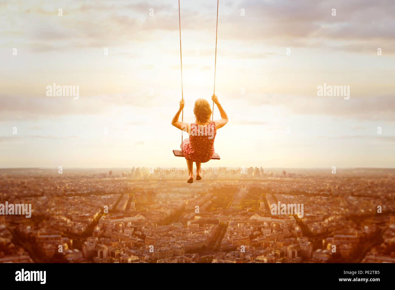 happiness and freedom concept, happy romantic beautiful young girl on the swing above the city landscape, cityscape at sunset, dream, joy and inspirat Stock Photo