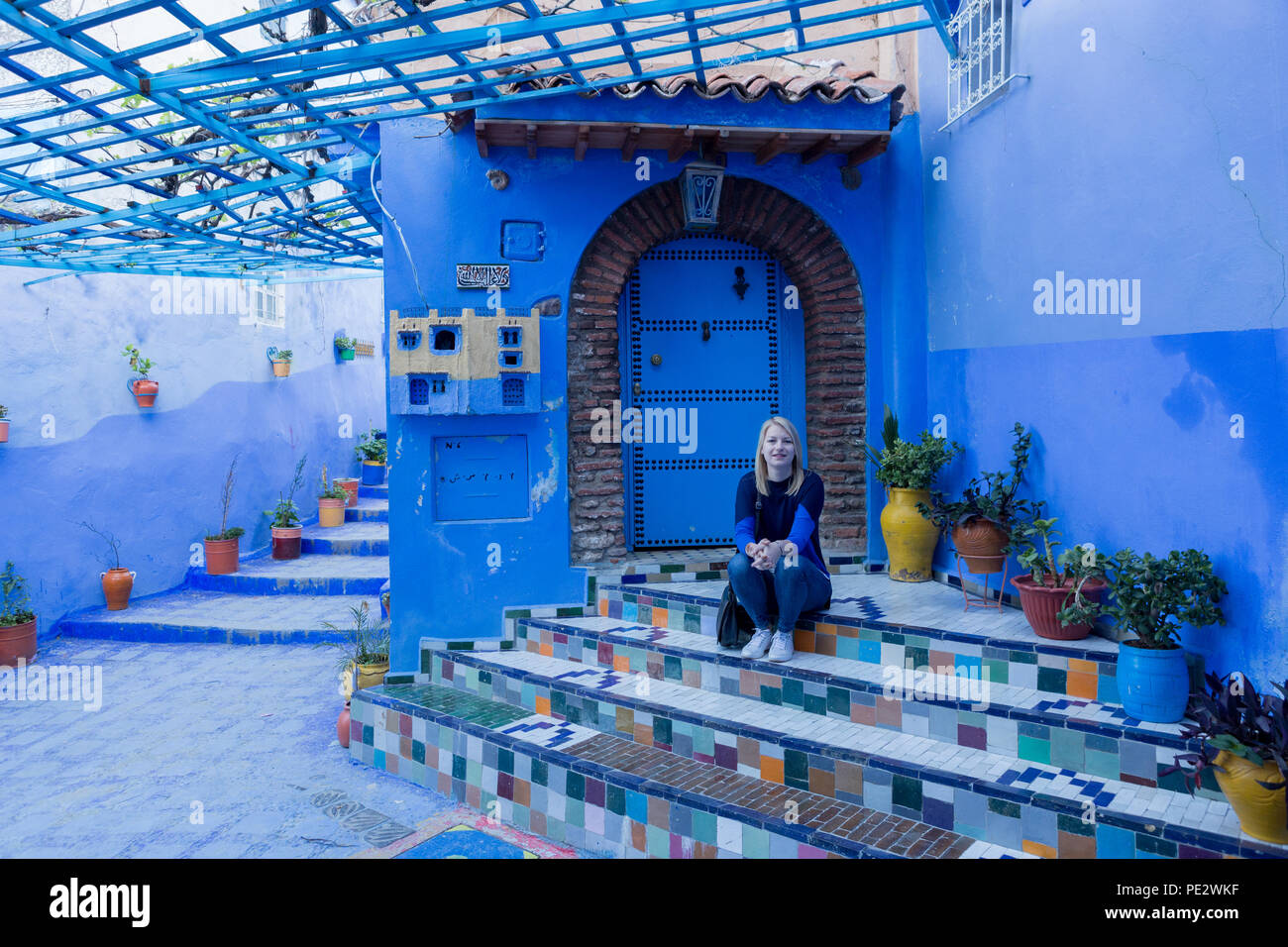 Blond girl is visiting in Chefchaouen (Chaouen) city in Morocco noted for its buildings in shades of blue. Stock Photo