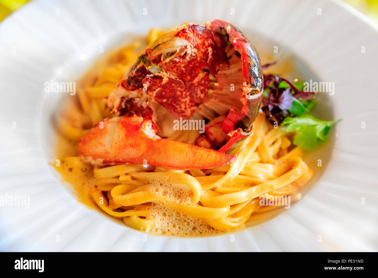 Linguine pasta with foam and lobster tail and claw on a half shell, decorated with parsley at a