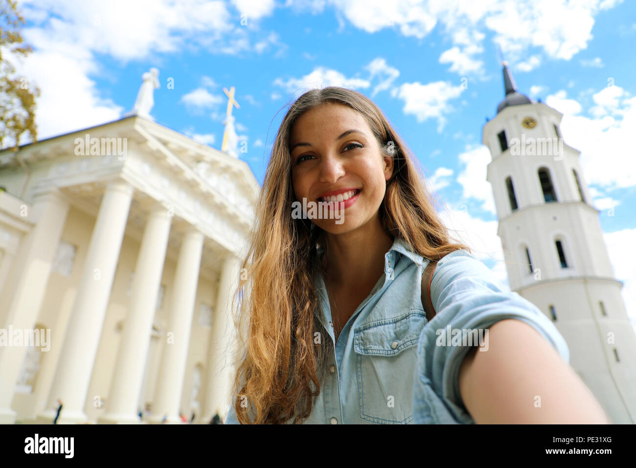 Happy smiling girl taking selfie picture in front of Vilnius Cathedral, Lithuania. Beautiful young woman traveling in Europe. Stock Photo