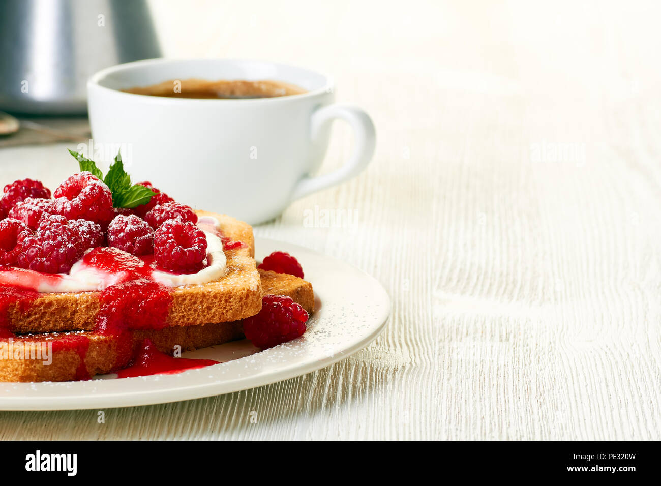 Coffee and toast with fresh raspberries on white table Stock Photo