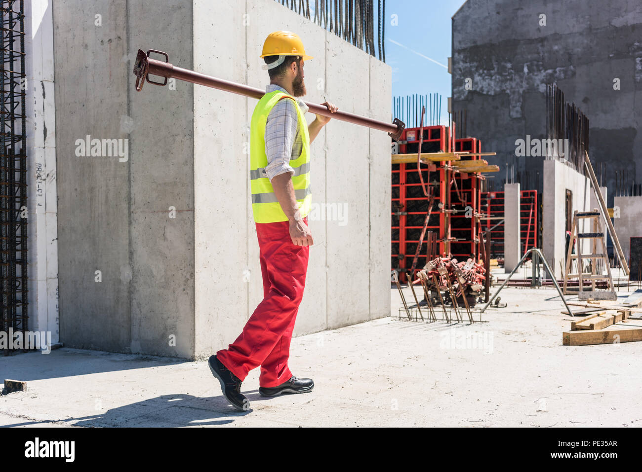 Bluecollar worker carrying a heavy metallic bar during work Stock