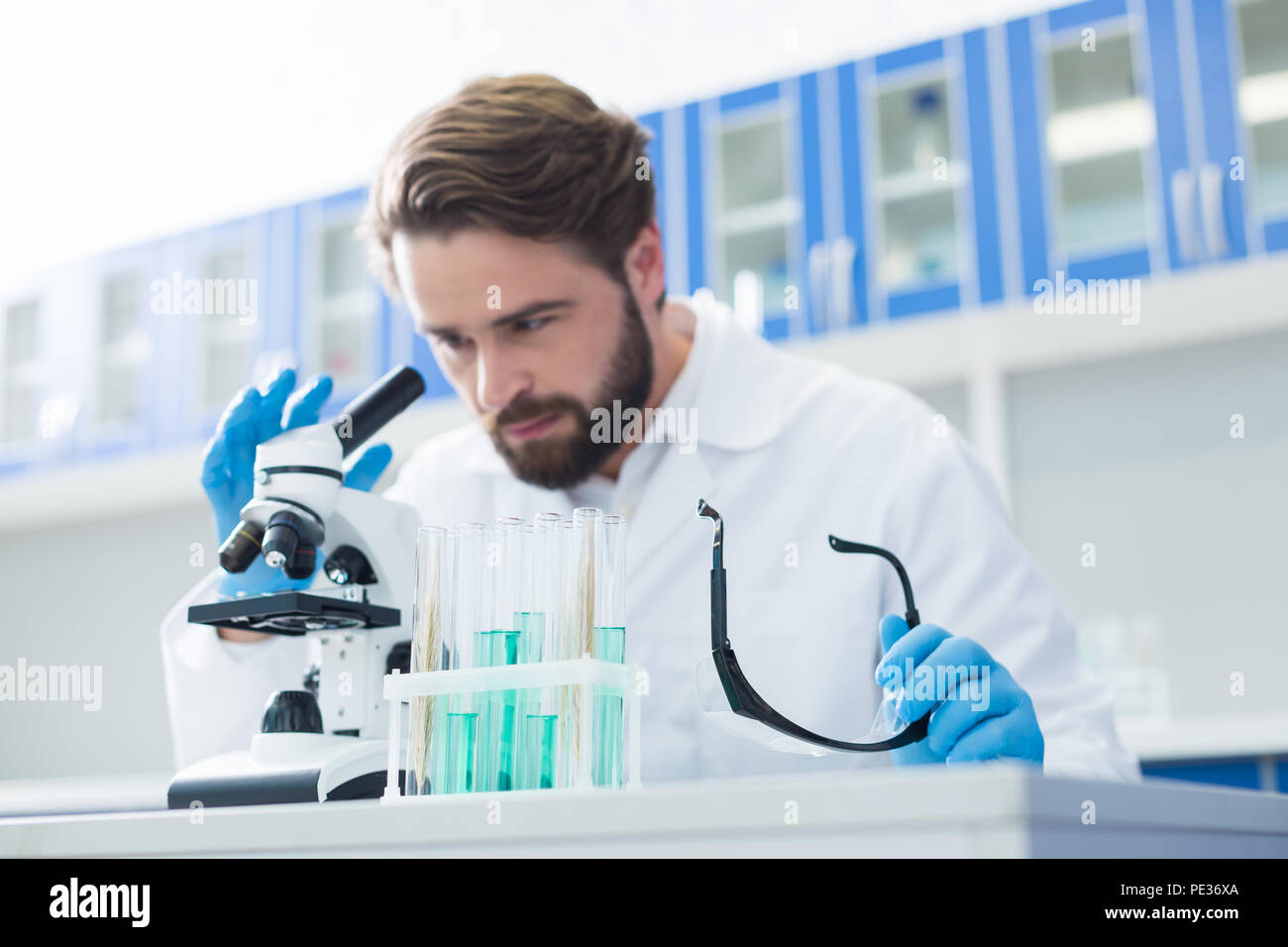 Chemical lab. Selective focus if test tubes standing on the table with a handsome professional chemist working in the background Stock Photo
