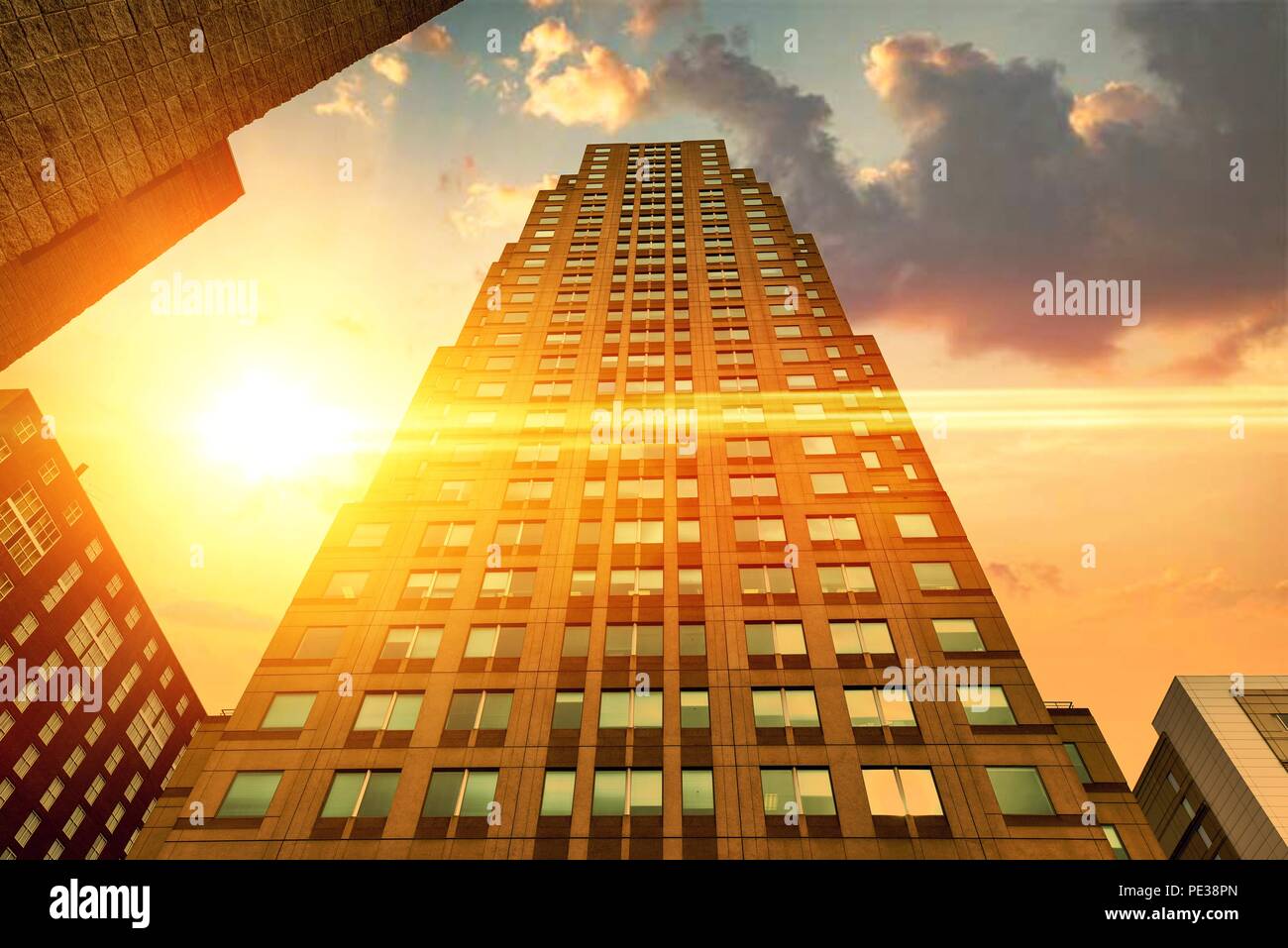 A wide angle closeup of a towering modern skyscraper with a dramatic sunset with light rays. Stock Photo