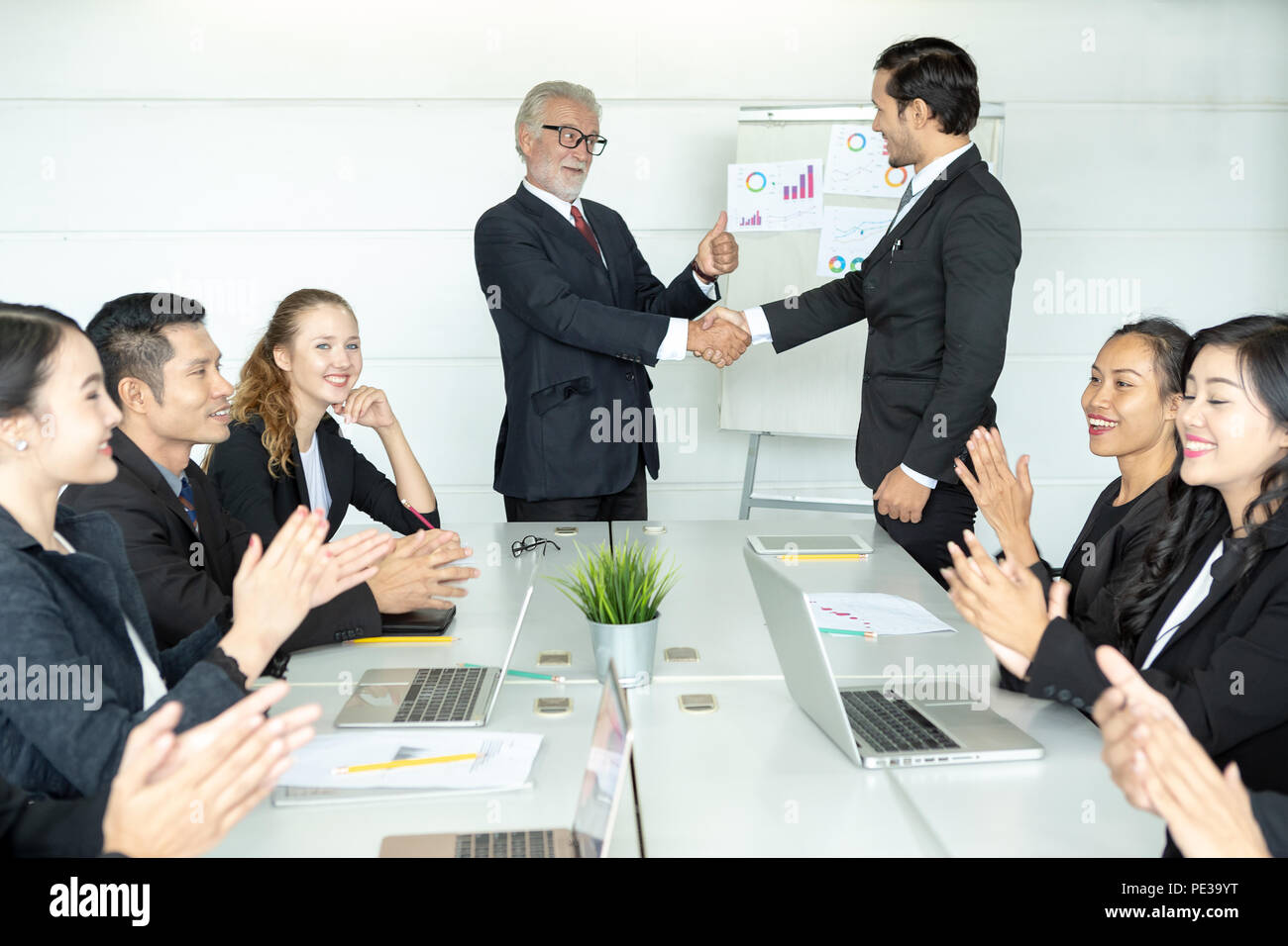 Senior Boss or CEO promoting young subordinate. Two businessmen handshaking, congratulating on promotion. Celebration of promotional event. Stock Photo