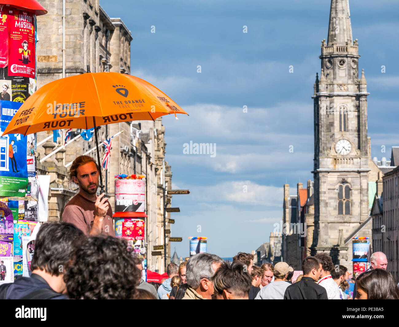 Man advertising free orange tour under umbrella with Tron Kirk spire and clock tower, Royal Mile, Edinburgh, Scotland, UK during Fringe festival Stock Photo