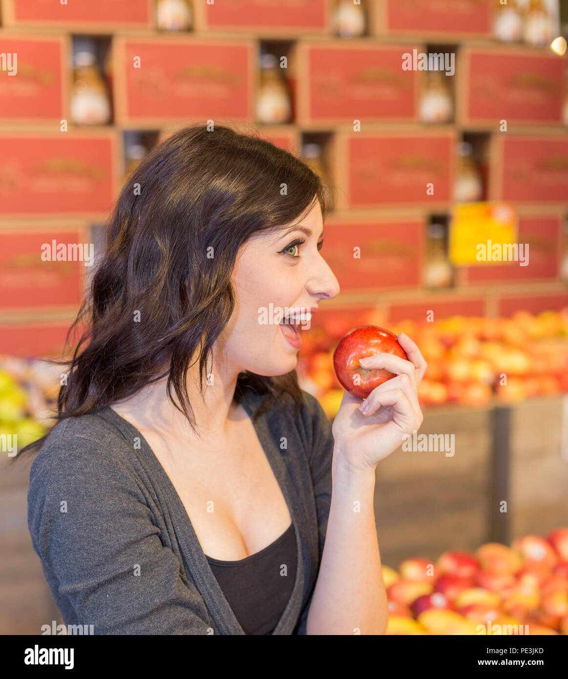 Girl in grocery store holding a red apple while smiling. Stock Photo