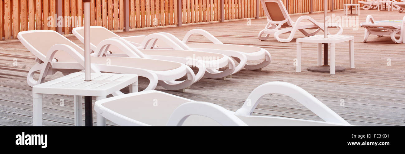 Banner Wooden deck beach sea ocean resort sun lounger umbrella hotel pool sky sunrise. Relax by the sea on the wooden terrace sunset evening Stock Photo