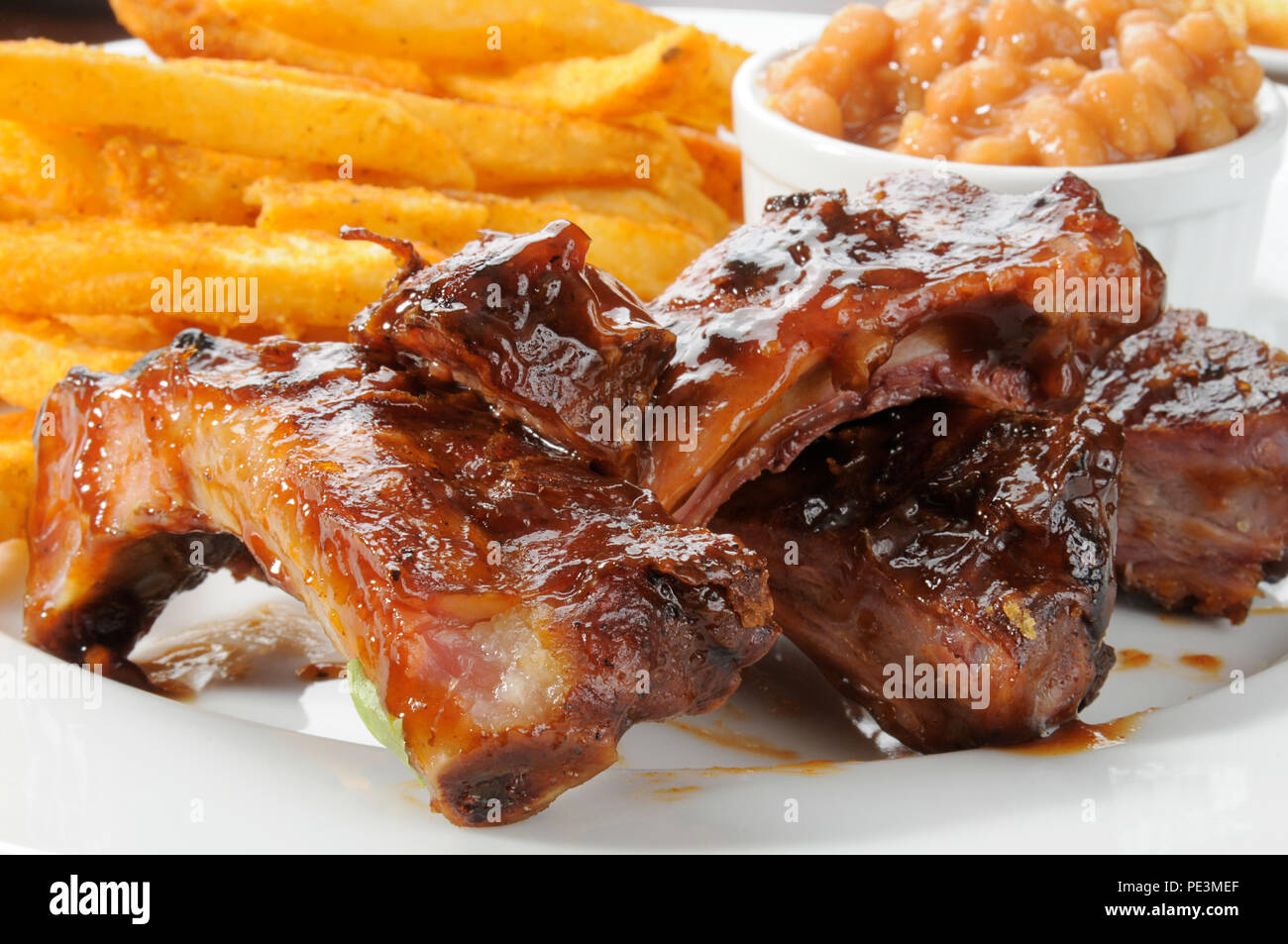 Close up of beef or pork ribs with fries and baked beans Stock Photo