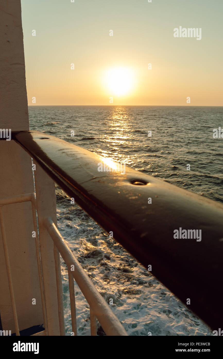 wooden railing of vessel in front of sea and sunset Stock Photo