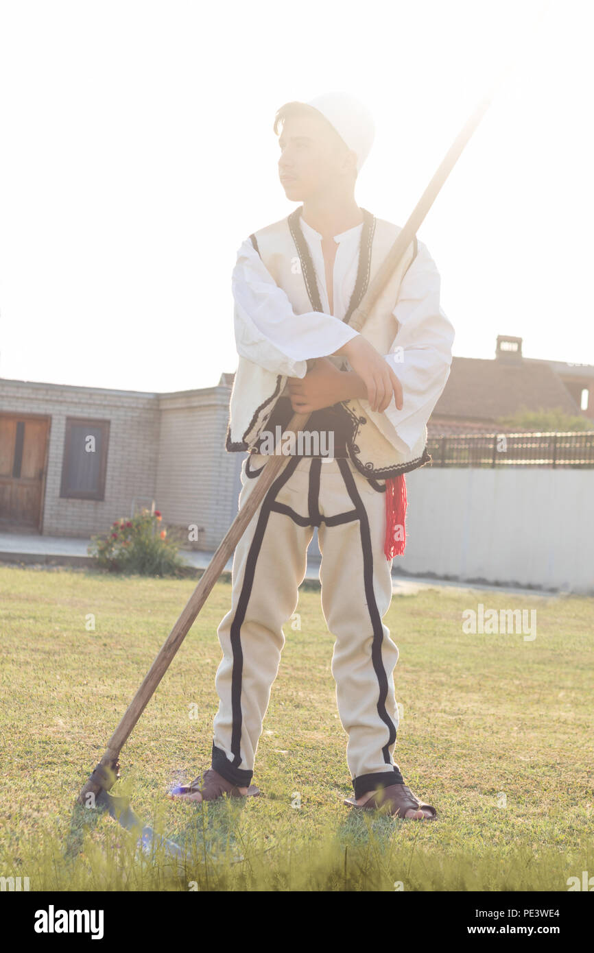 young man in traditional costume mow the grass with scythe in the old way Stock Photo
