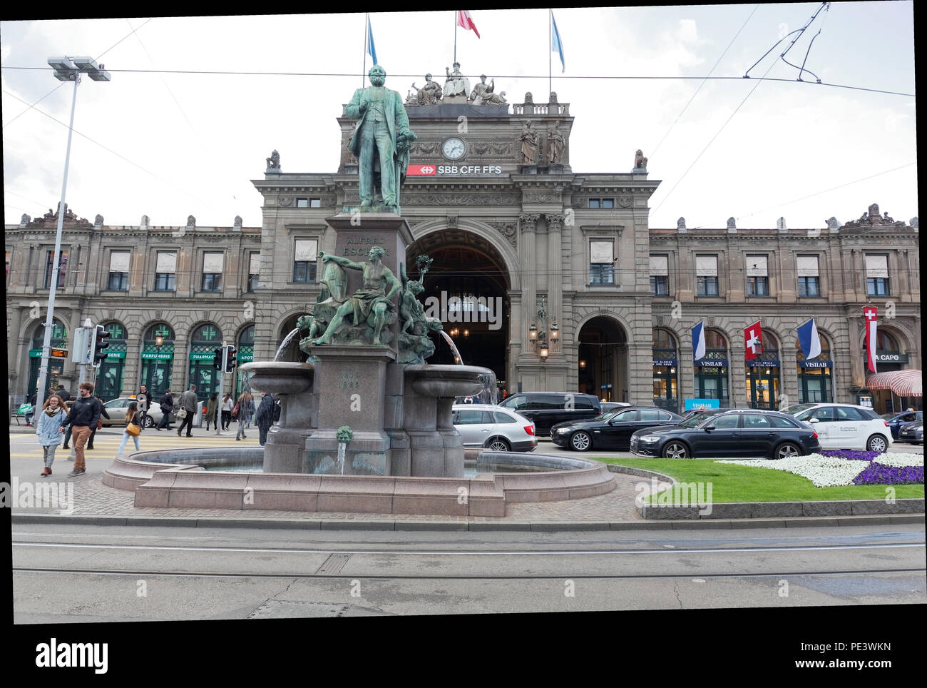 Monument of Alfred Escher on Bahnhofplatz square,Zurich main train station building in the background. He was a Swiss businessman and railways pioneer Stock Photo