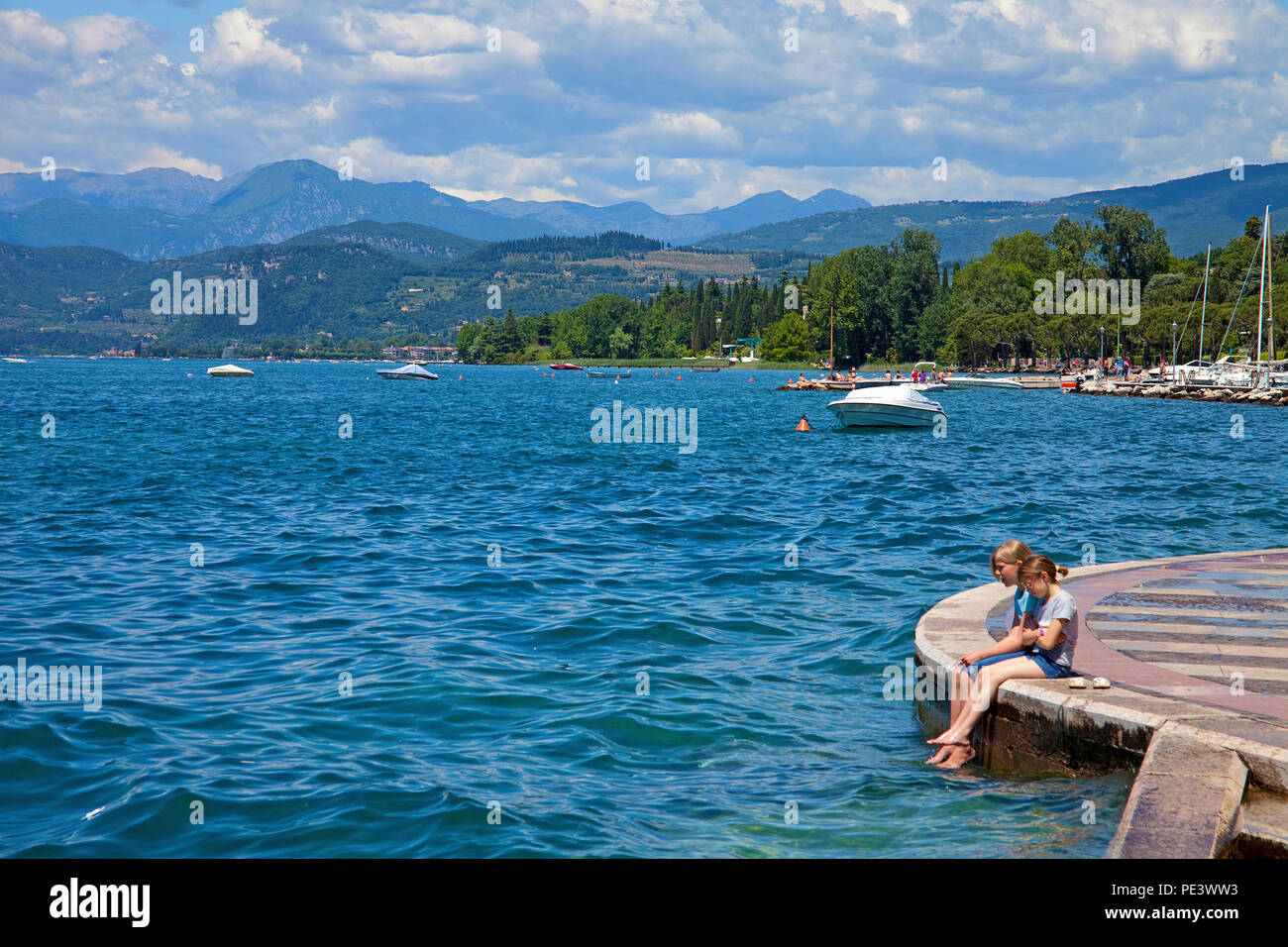Two young girls sitting at lake promenade of Lazise, Garda lake, province Verona, Italy Stock Photo