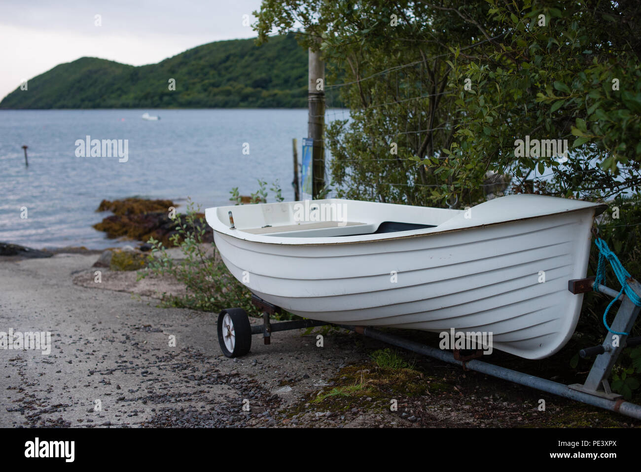 Small white rowing boat constructed in fibre glass to reflect traditional wooden vessels with its trailer on slipway by the sea Stock Photo