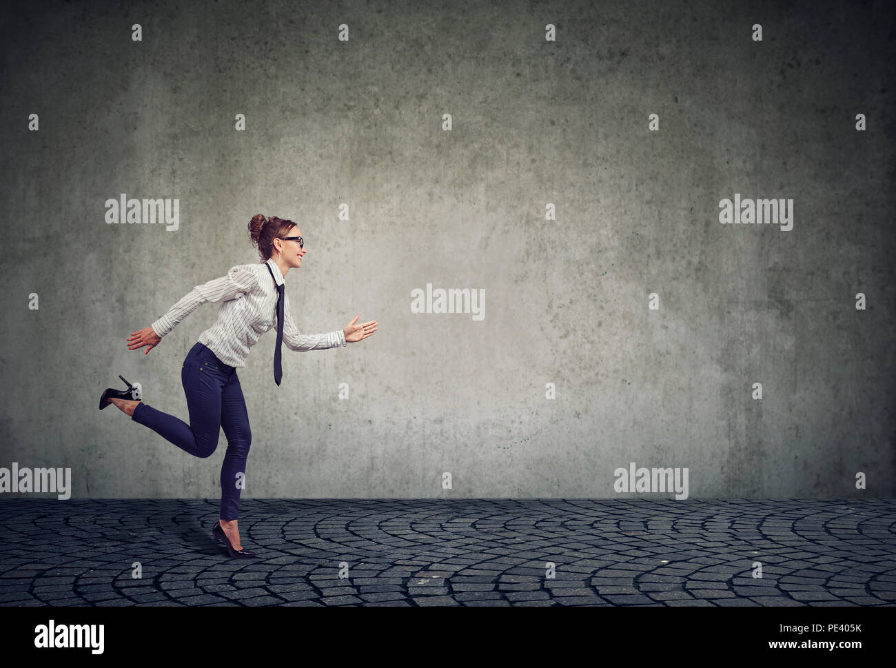 Side view of modern formal business woman running forward under time pressure willing to manage professional competition against gray wall Stock Photo