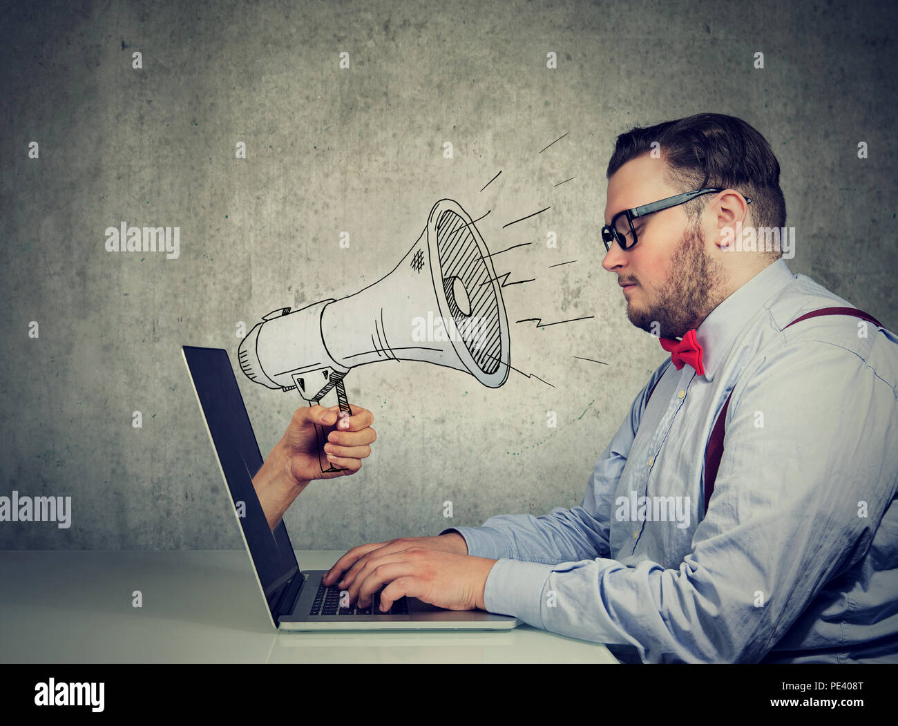 Businessman sitting at table working on computer screaming with a megaphone poking out from a laptop screen Stock Photo