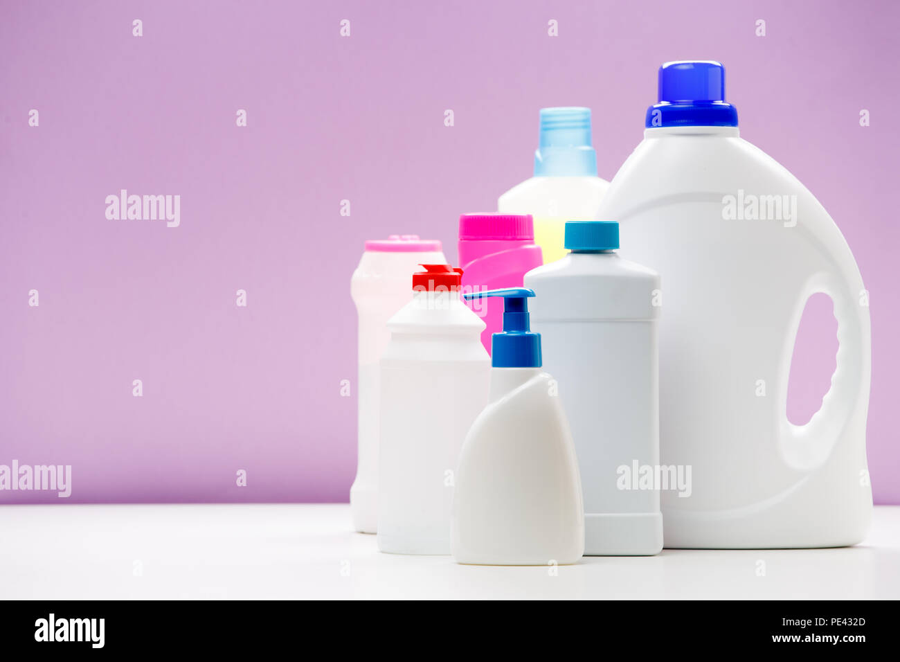Photo of bottles of cleaning products on white table isolated on purple background Stock Photo
