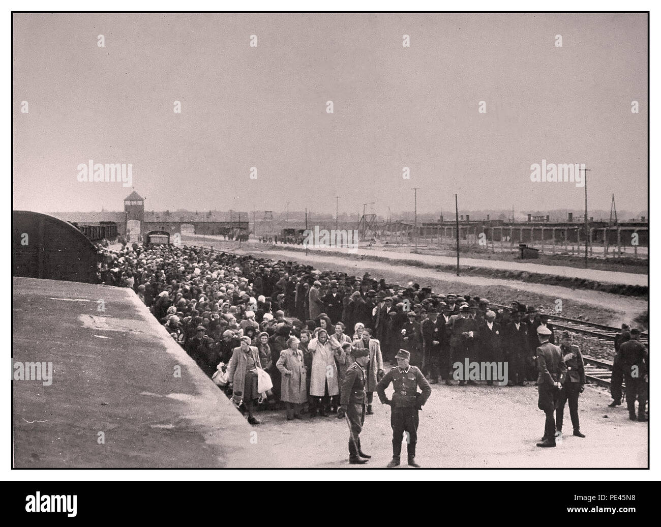AUSCHWITZ-BIRKENAU HOLOCAUST PRISONERS ARRIVAL- A vision of hell on earth. 1944.  Nazis Troops in military uniform wearing jackboots  'grading' (life or death) unsuspecting male and female prisoners on rail concourse outside entrance to Auschwitz-Birkenau extermination death camp. The infamous Auschwitz camp was started by order of Adolf Hitler in 1940's during the occupation of Poland by Nazi Germany during World War 2. It was enthusiastically enabled by Heinrich Luitpold Himmler the Reichsführer of the Schutzstaffel, and leading member of the Nazi Party of Germany. Stock Photo