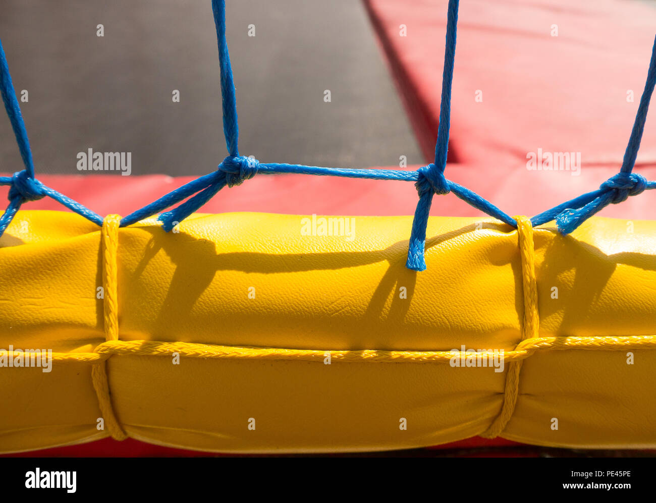 Colour close up of part of a red and yellow trampoline, with a blue net wall Stock Photo