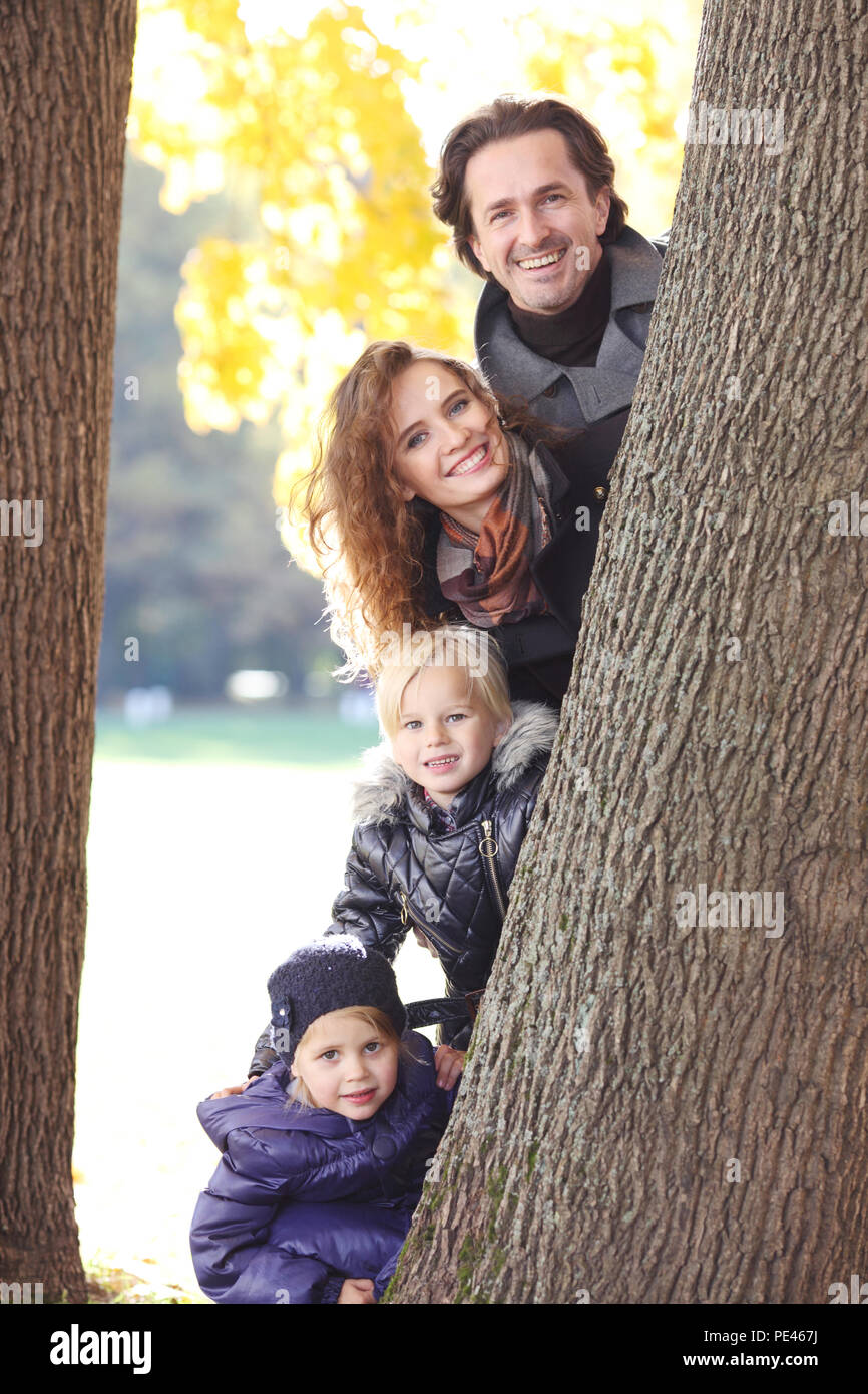 Happy smiling family of parents and children in autumn park standing near big tree trunk Stock Photo