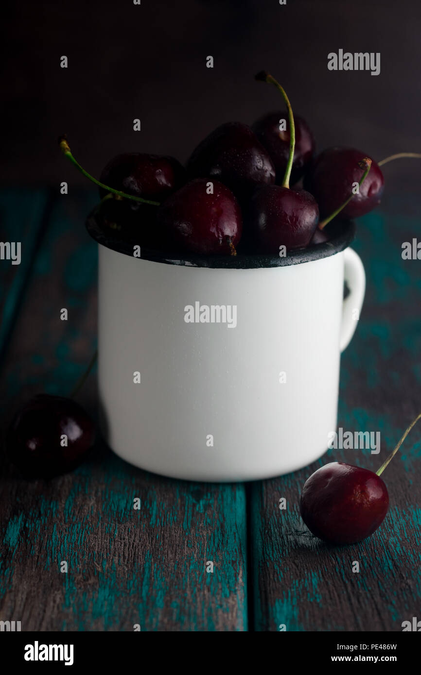 Cherries in tin cup on rustic wooden desk. Toned photo. Stock Photo