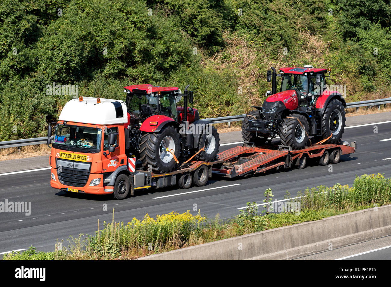 Flatbed truck with two farm tractors on motorway. Stock Photo
