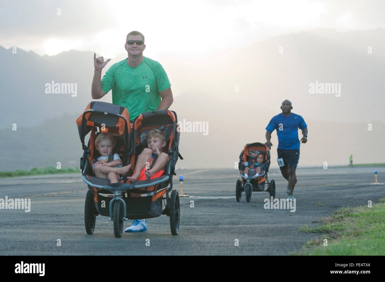 Staff Sgt. Greg Markley, the station captain for Aircraft Rescue and Firefighting, Marine Corps Air Station Kaneohe Bay and a Fort Myers, Fla., native pauses for a photo opportunity with his children while competing in the Sunset Flightline 5K aboard Marine Corps Base Hawaii, Sept. 18, 2015. More than 240 people participated in the evening race, which began and ended between Hangars 101 and 102. The Marines and Sailors of Marine Aircraft Group 24 partnered with Marine Corps Community Services Hawaii for the race, and a portion of the event’s net profits went to the unit. The race was open to t Stock Photo