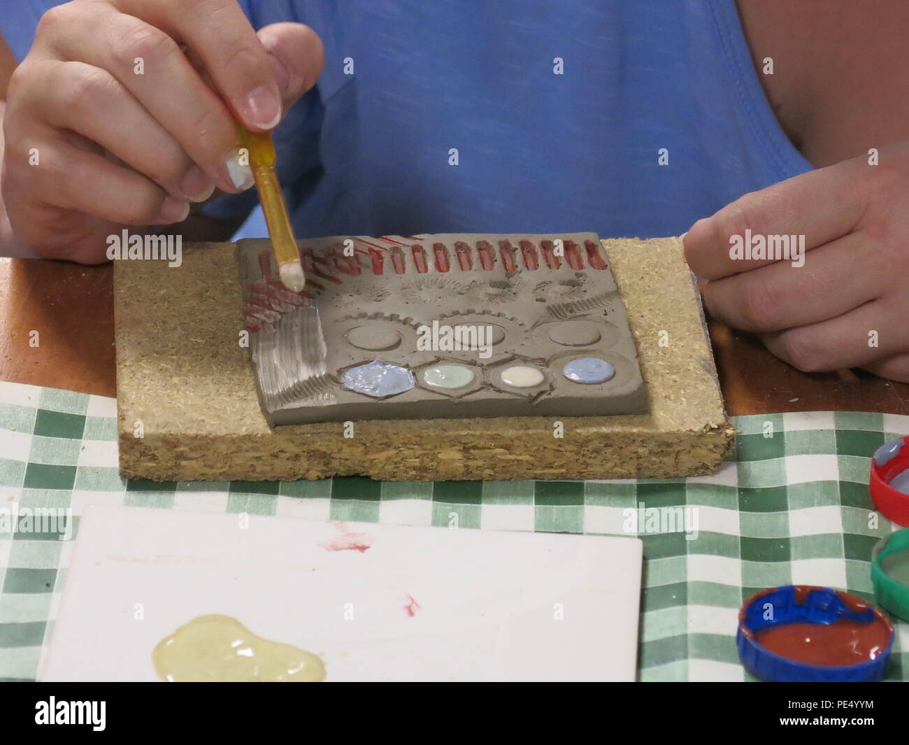 Close up of a child's hands designing and decorating a clay tile; craft