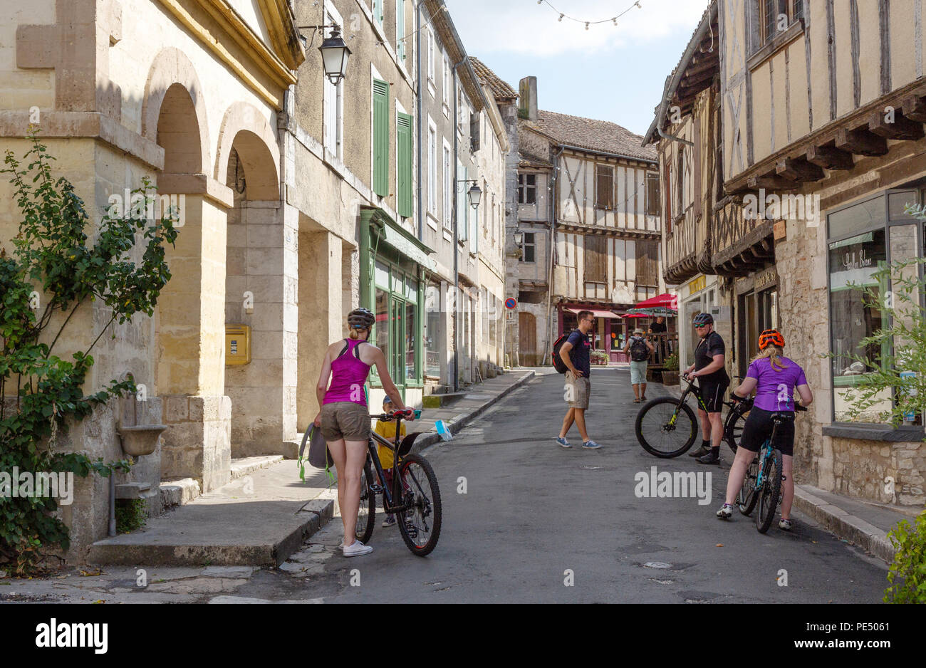 People cycling in the bastide town of Issigeac in the Dordogne, France Europe Stock Photo