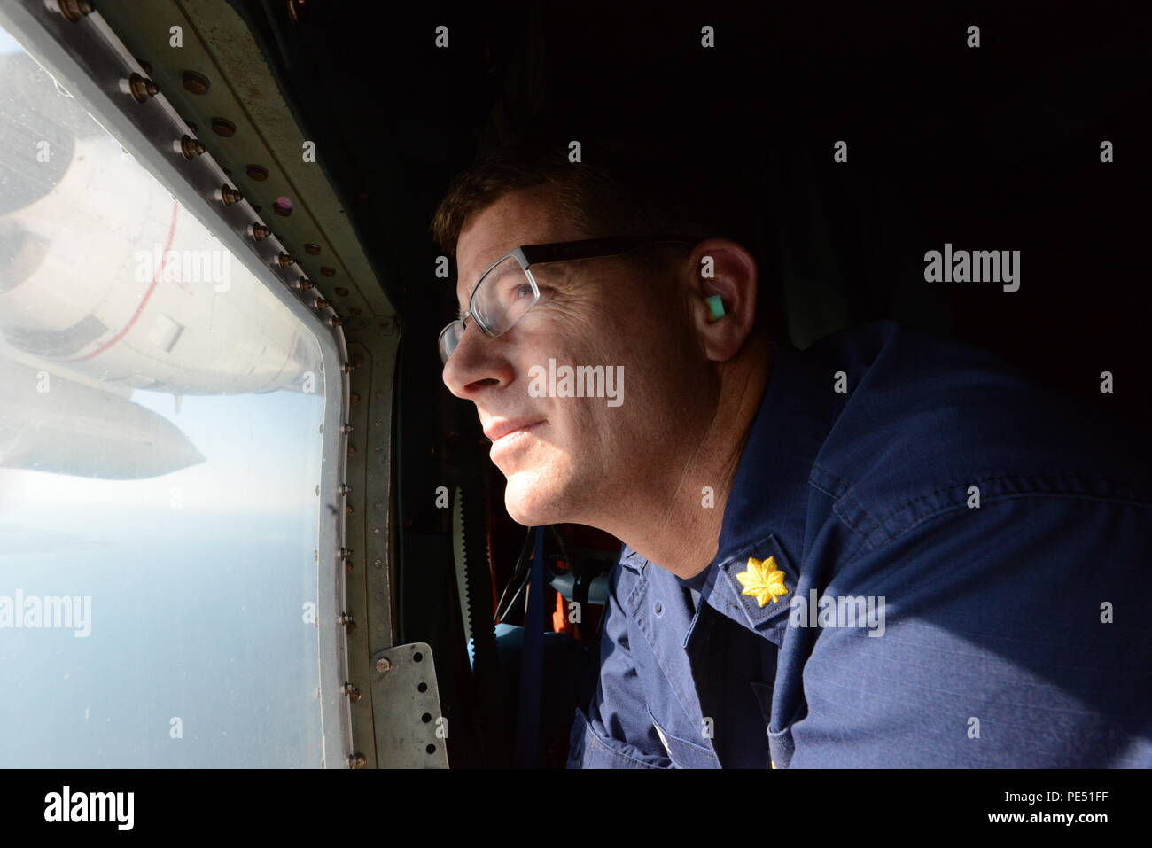 Lt. Cmdr. Todd Boze peers out of a window of an HC-130 Hercules aircraft during a fisheries surveillance flight of the Pacific Northwest, Sept. 30, 2015. During the flight, the crew identified and documented 32 commercial fishing vessels in support of the Coast Guard's Living Marine Resources mission and partner agencies. (U.S. Coast Guard photo by Seaman Sarah Wilson) Stock Photo