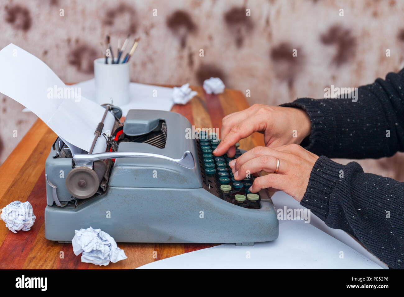 The man in a sweater typing on an old-fashioned typewriter. On the table are glasses and there is a mug Stock Photo