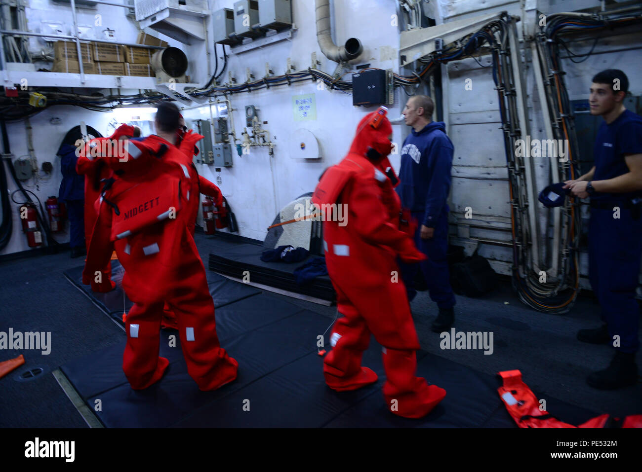 Crew members aboard the Coast Guard Cutter Midgett, a 378-foot high-endurance cutter homeported in Seattle, put on immersion suits during underway training, Oct. 9, 2015. Immersion suits are suits that crew members would put on in case they had to abandon ship. (U.S. Coast Guard photo by Petty Officer 1st Class Levi Read Stock Photo