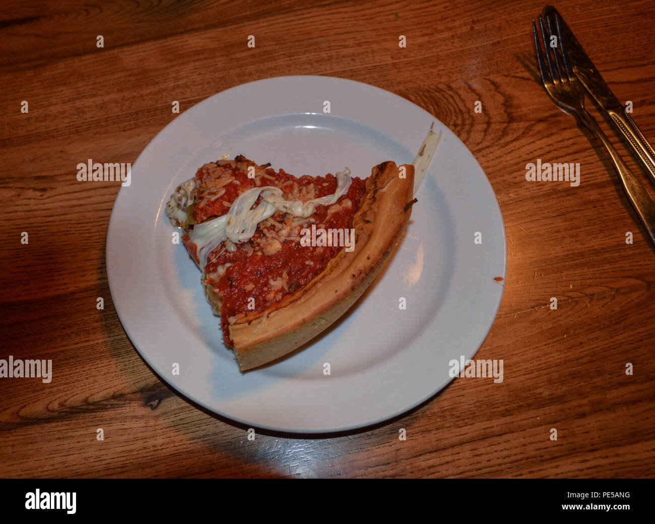Dining Out A Thick Delicious Slice Of Traditional Chicago Style Baked Italian Stuffed Famous Pizza Food Meal On a Round White Plate with Silverware Stock Photo