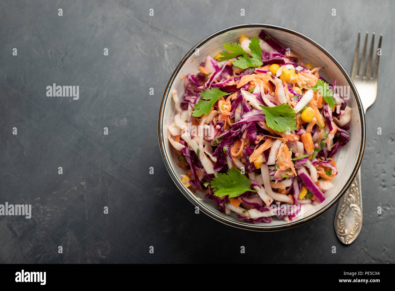 Purple cabbage and carrot salad with mayonnaise in a white bowl on a black background. Classic coleslaw. Diet vegetarian dish. Top view with copy space Stock Photo