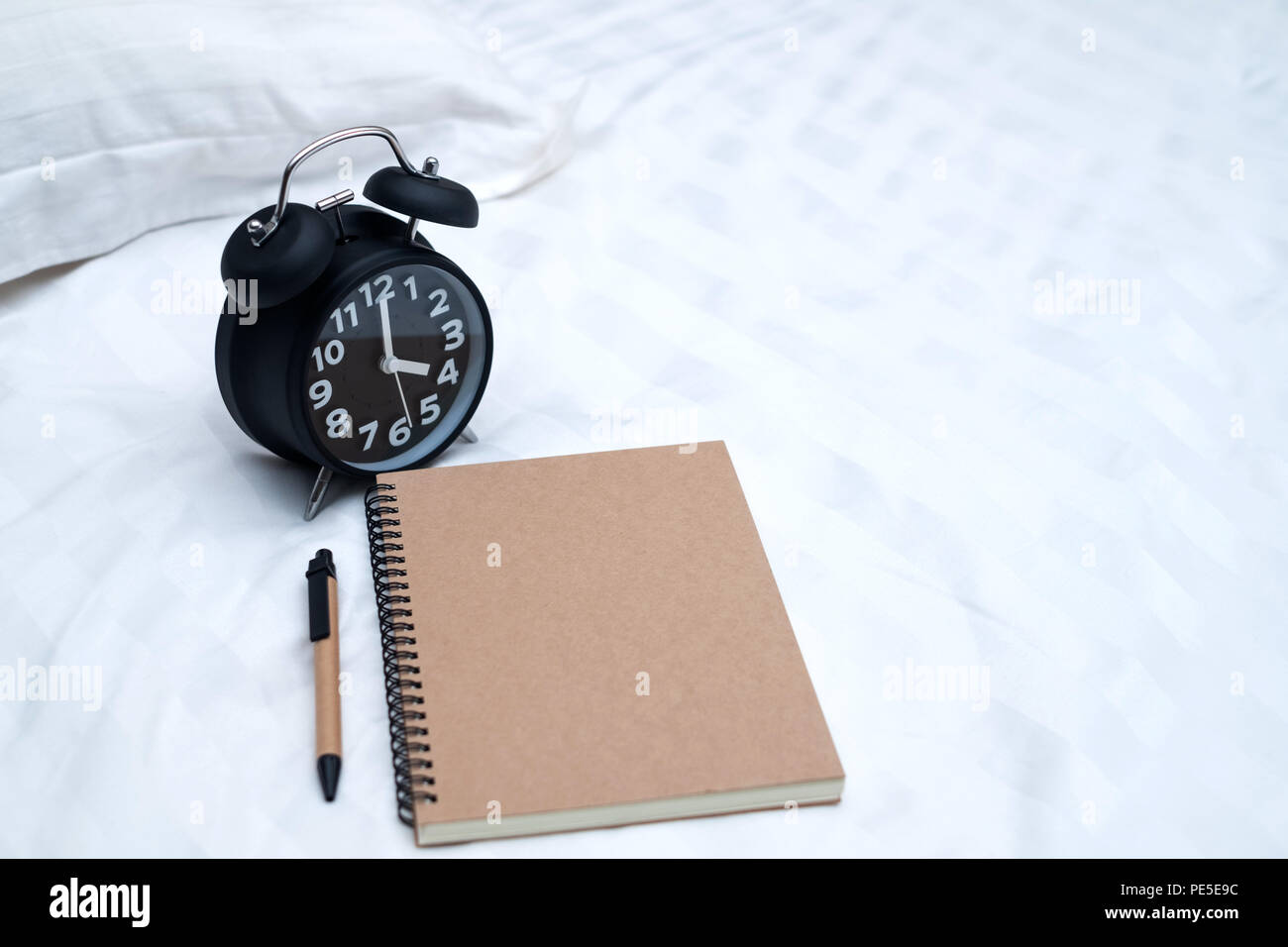 Diary or notebook and vintage alarm clock on bed in bedroom at home or hotel, working or note something before sleep. Stock Photo