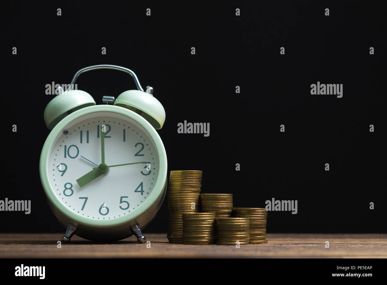Alarm clock and coins stacks on working table in dark room, time for ...