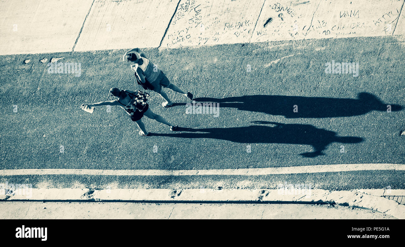 Silhouette of a two womans casting a long shadow on a asphalt road ...