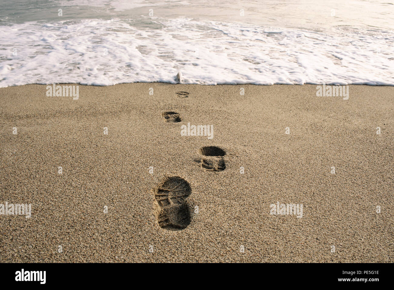 Swallowed in the sea. Shoe footprints in sand. Expressive conceptual imagery. Punta Hermosa, Lima District, Peru. Jul 2018 Stock Photo