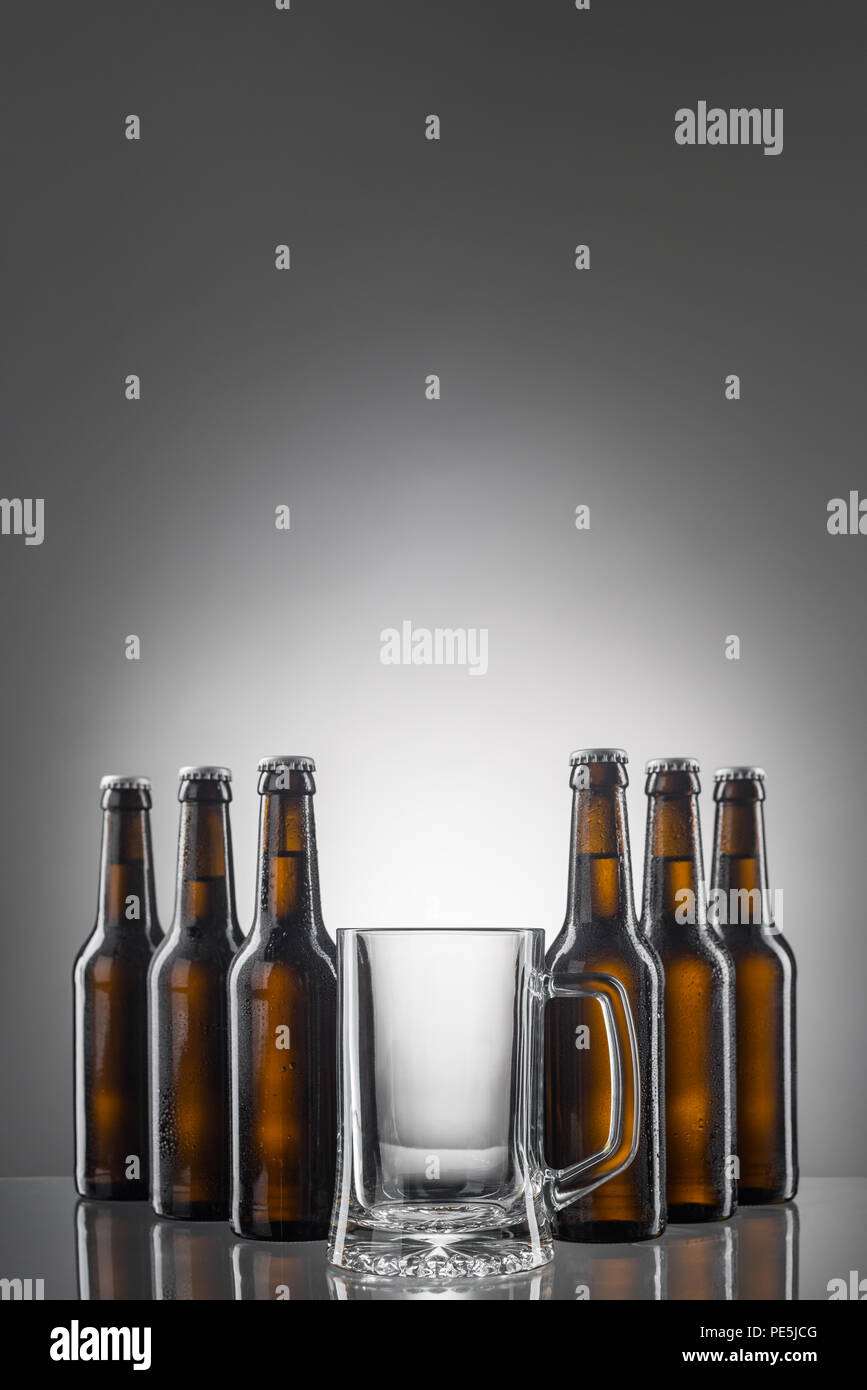 Six beer bottles and big empty cup. Reflections on glossy table. Vertical shot with big copy space to insert your text. Stock Photo