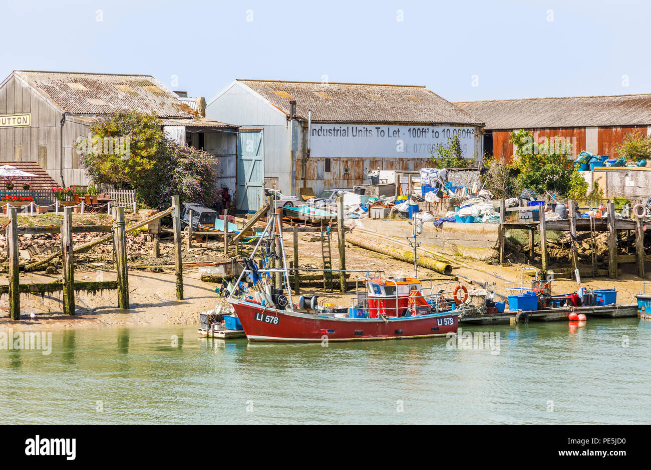 Red fishing boat moored by industrial units on the riverbank on the West Beach side of the River Arun estuary, Littlehampton, south coast West Sussex Stock Photo